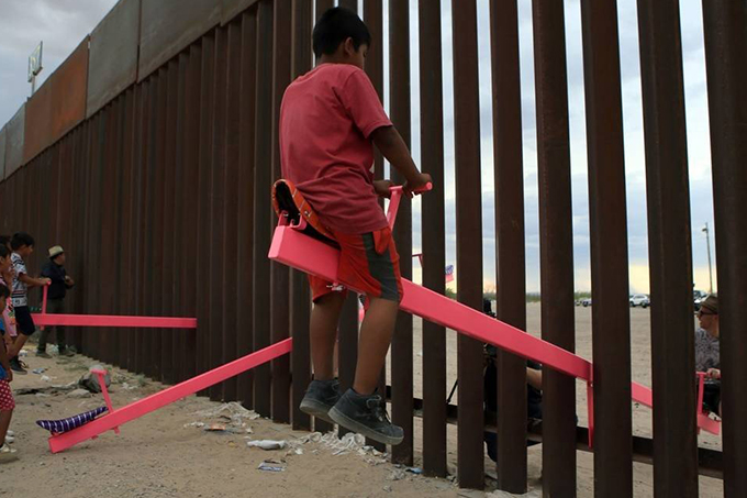 Gangorra é instalada na cerca entre EUA e México e crianças brincam juntas